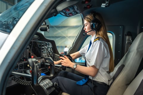 Young woman pilot using a smartphone while seated in the cockpit of a private plane, skillfully managing communication and navigation